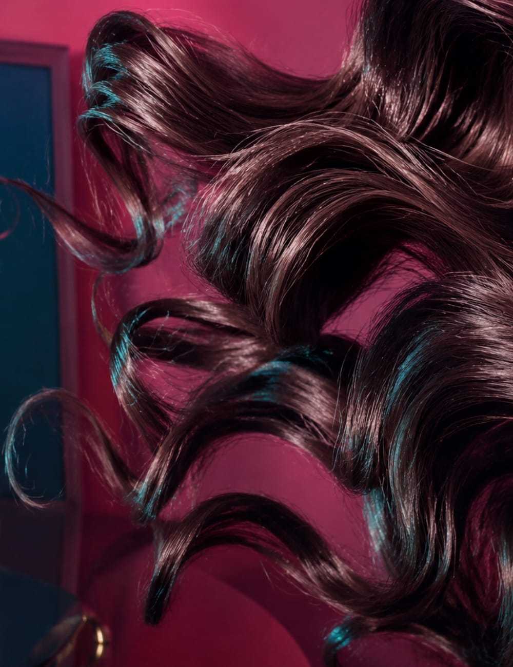 Flowing dark hair in soft curls against a vibrant pink background.
