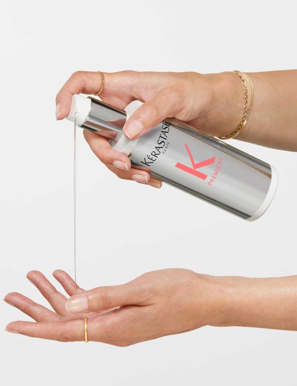 Hands pouring Kérastase hair product onto palm, showcasing packaging and product texture.