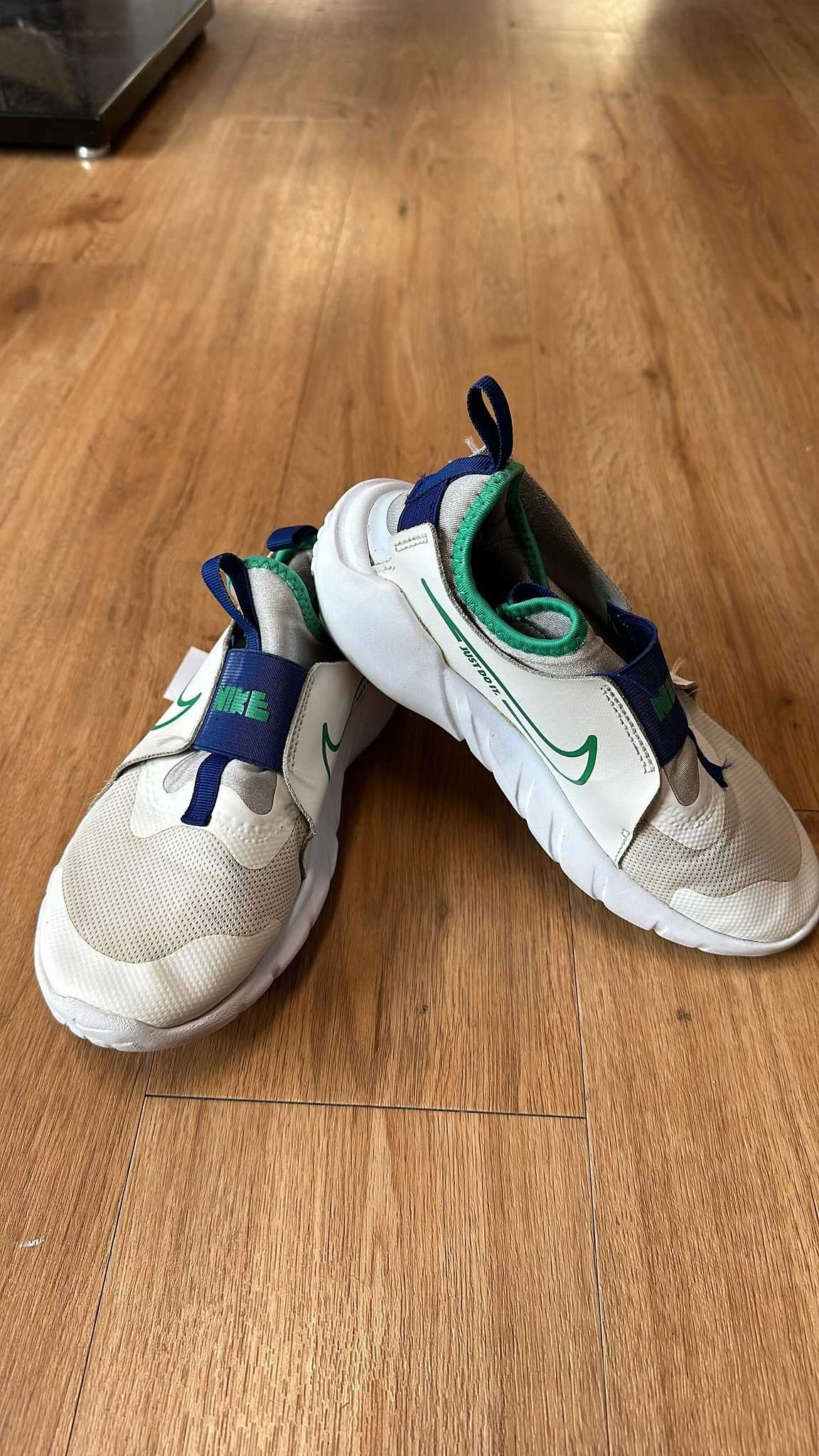 Two beige and green athletic shoes with white soles on a wooden floor.