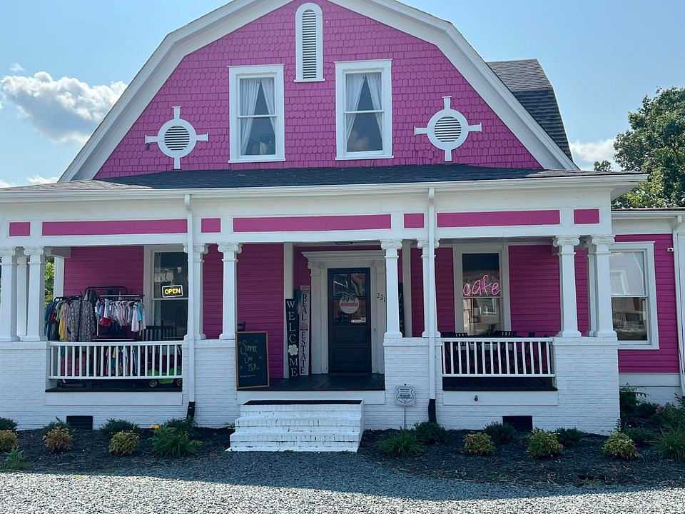 Pink and white storefront with clothes rack, "Open" sign, and "Welcome" sign on porch.