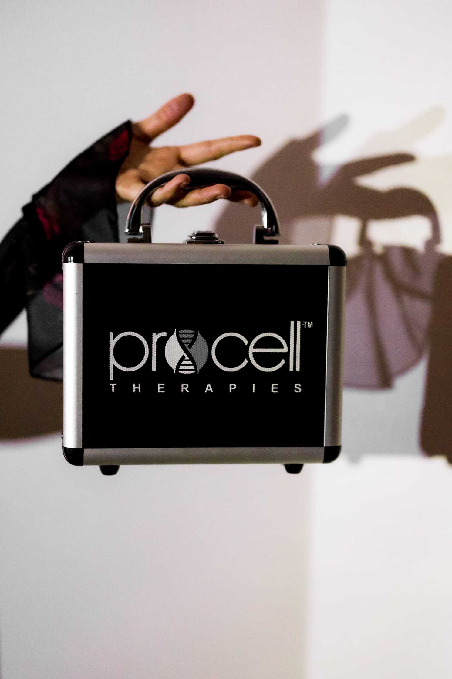 A hand holding a black Procell Therapies case with a shadow in the background.