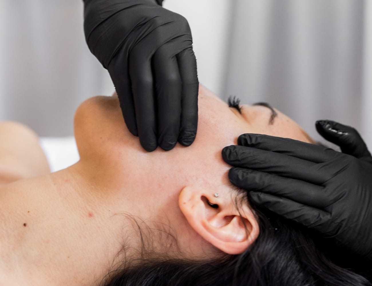 Facial massage with black gloves on a relaxed person's face.