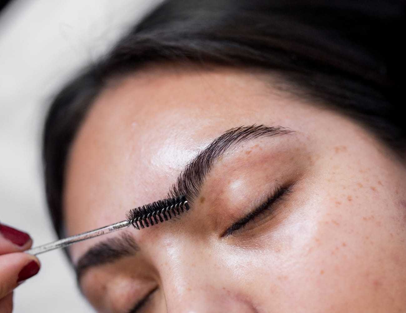 Close-up of a person having an eyebrow grooming process with a brush tool.