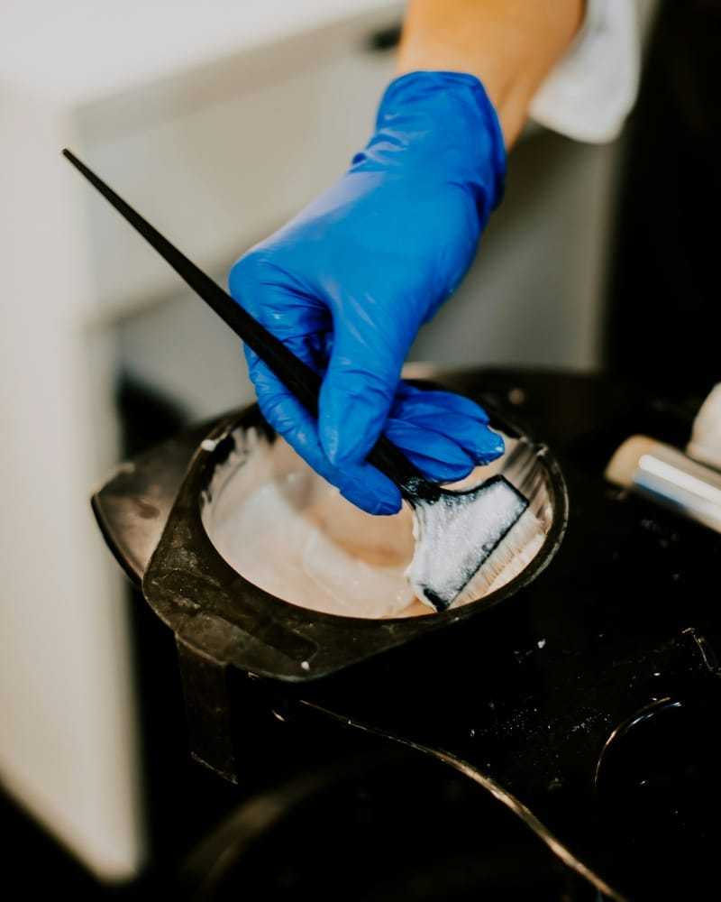 Hair dye being mixed in a bowl with a brush by a person wearing blue gloves.