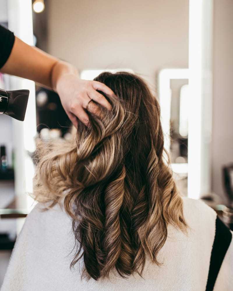 Hair stylist curling woman's hair in a salon with curling iron.
