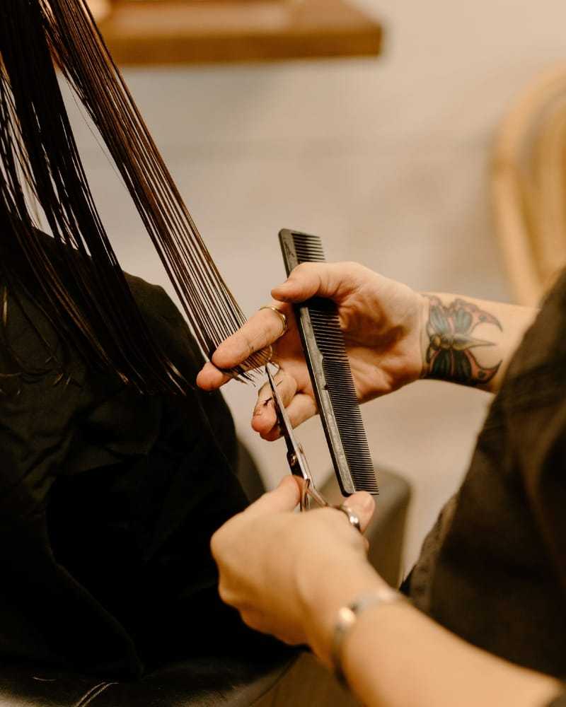 Hairdresser trimming long brown hair with scissors and comb in a salon.